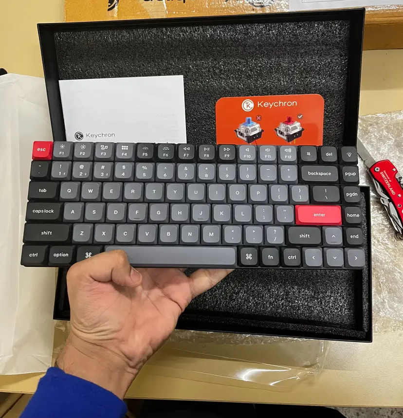 Keychron K3 Pro mechanical keyboard being held above its packaging